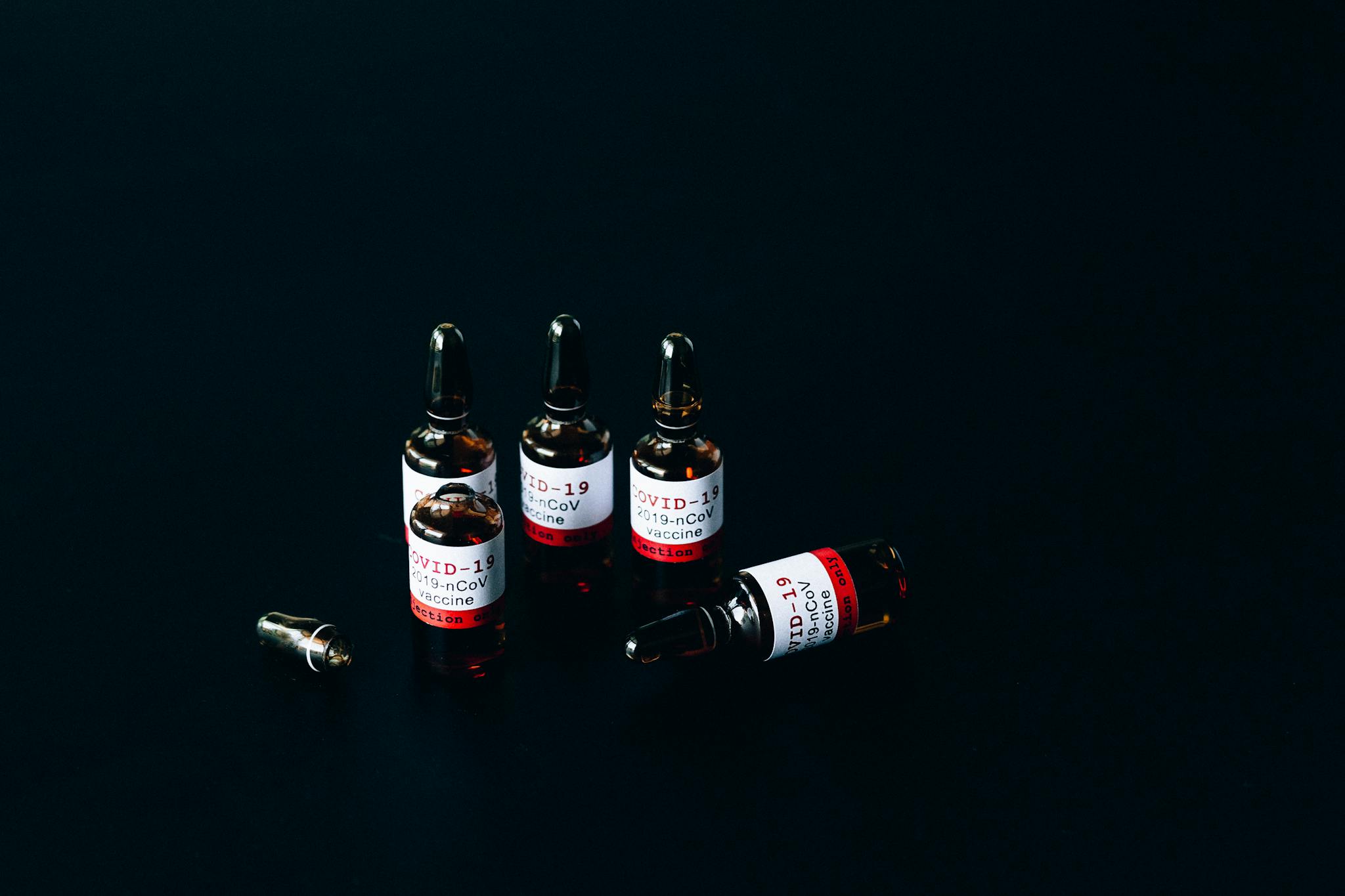 Close-up of COVID-19 vaccine vials on dark surface reflecting modern healthcare challenges.