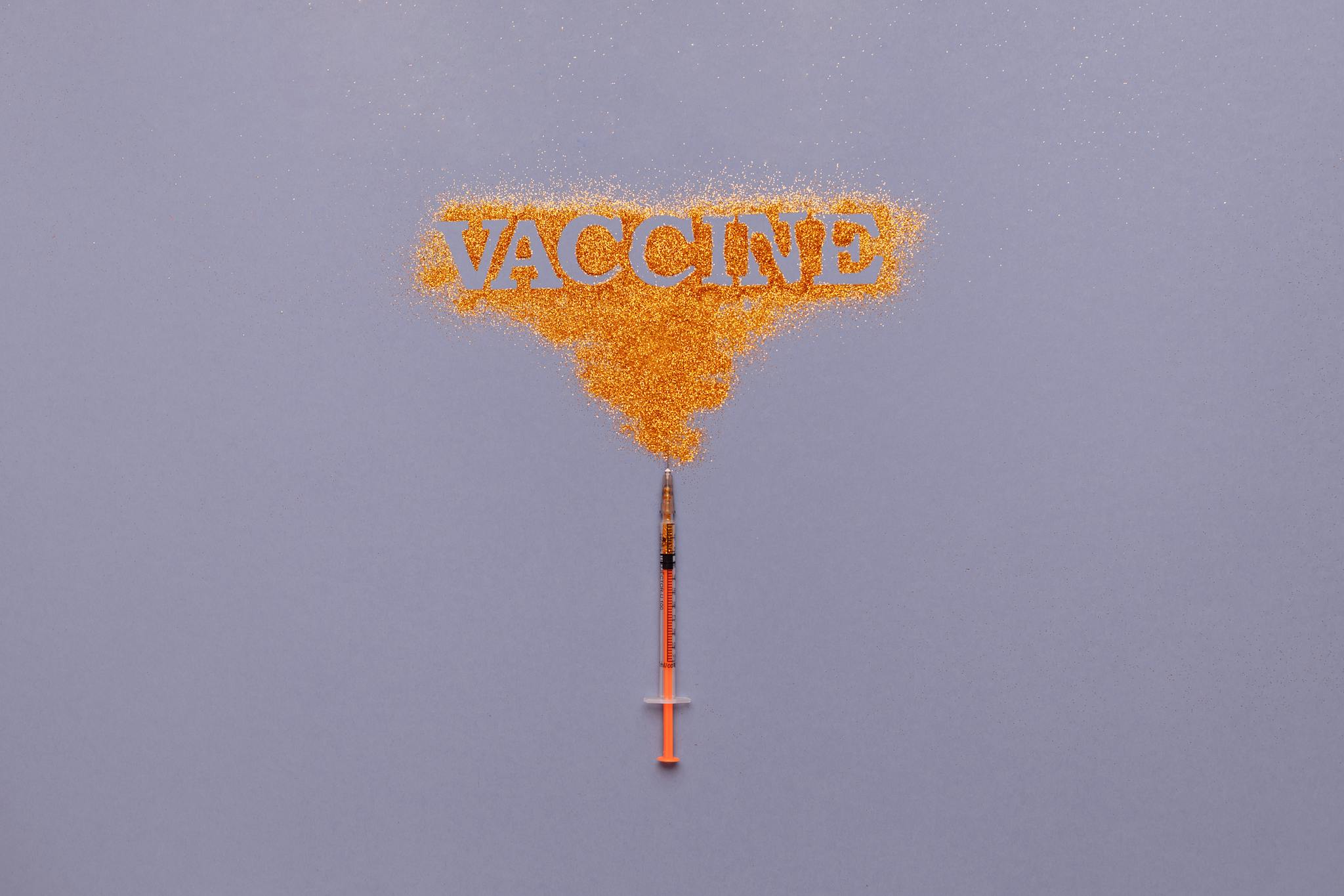 Conceptual image of a syringe with the word 'vaccine' in orange powder on a gray background.